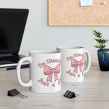 Two white mugs with pink bows and text on a desk with office supplies.
