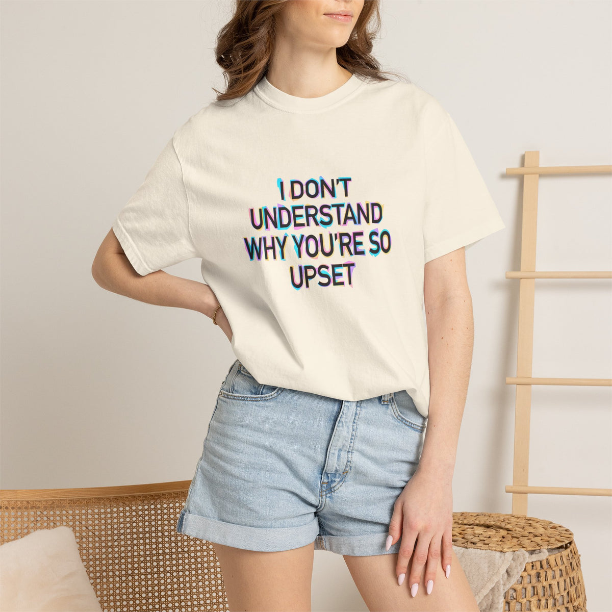 Woman wearing a beige t-shirt with colorful text "I don't understand why you're so upset" and denim shorts in a casual setting.