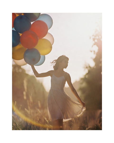 whimsical photography poster of a young woman holding colorful balloons in a field with a warm glow