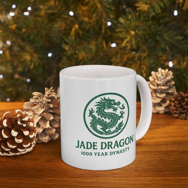 White mug with green dragon design and text on a wooden surface with pinecones and a Christmas tree in the background