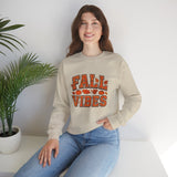 Woman wearing a beige sweatshirt with 'Fall Vibes' text, sitting on a white surface with a plant in the background.