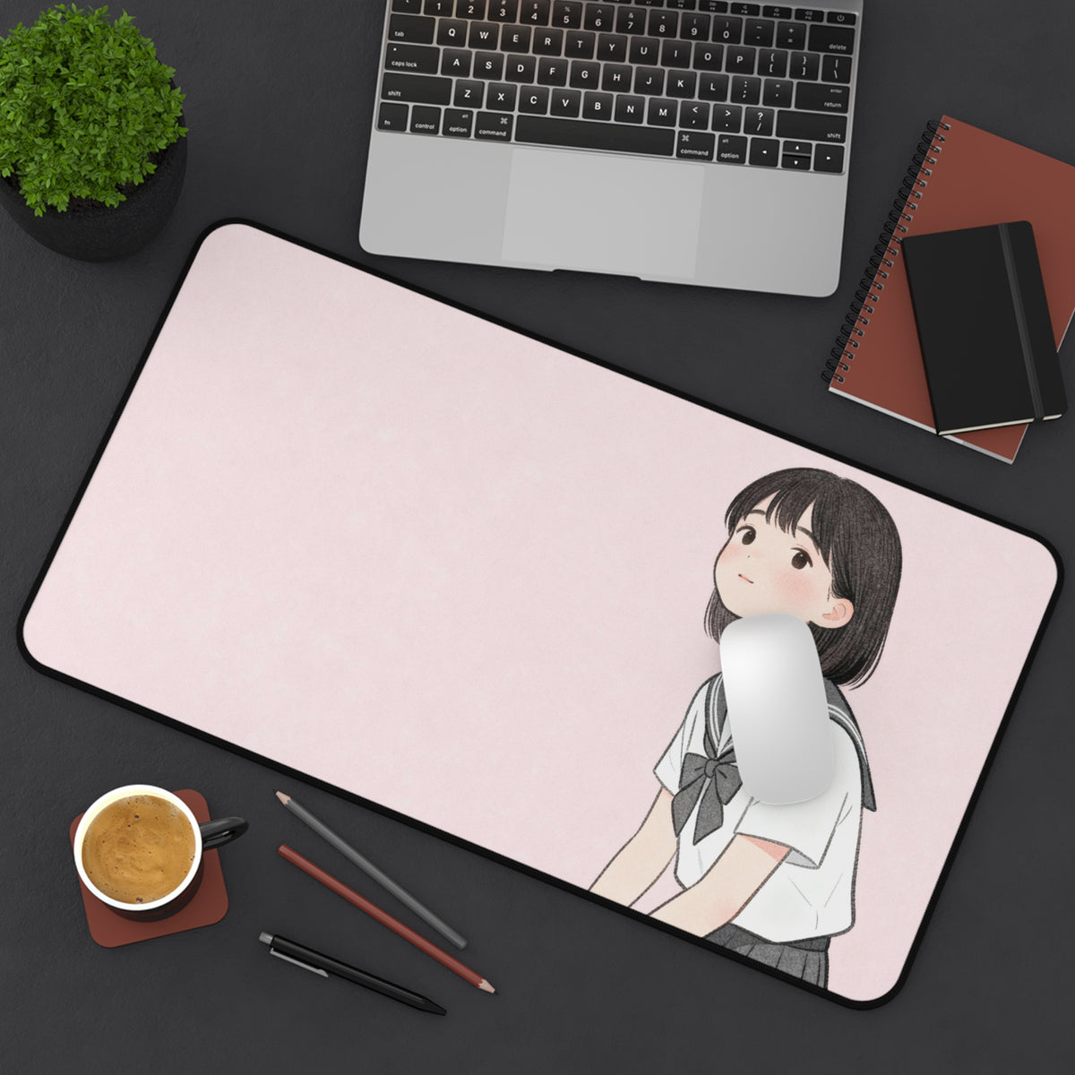Desk setup with a large mouse pad featuring an illustration of a Japanese girl student, a laptop, notebook, and coffee cup on a dark surface.
