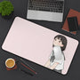 Desk setup with a large mouse pad featuring an illustration of a Japanese girl student, a laptop, notebook, and coffee cup on a dark surface.