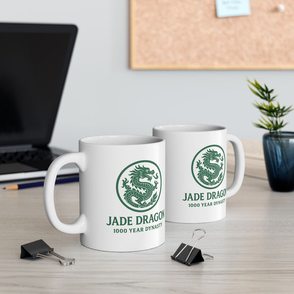 Two white mugs with green dragon logo on a desk with office items.