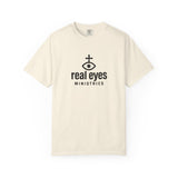 Beige t-shirt with 'real eyes ministries' logo on a white background