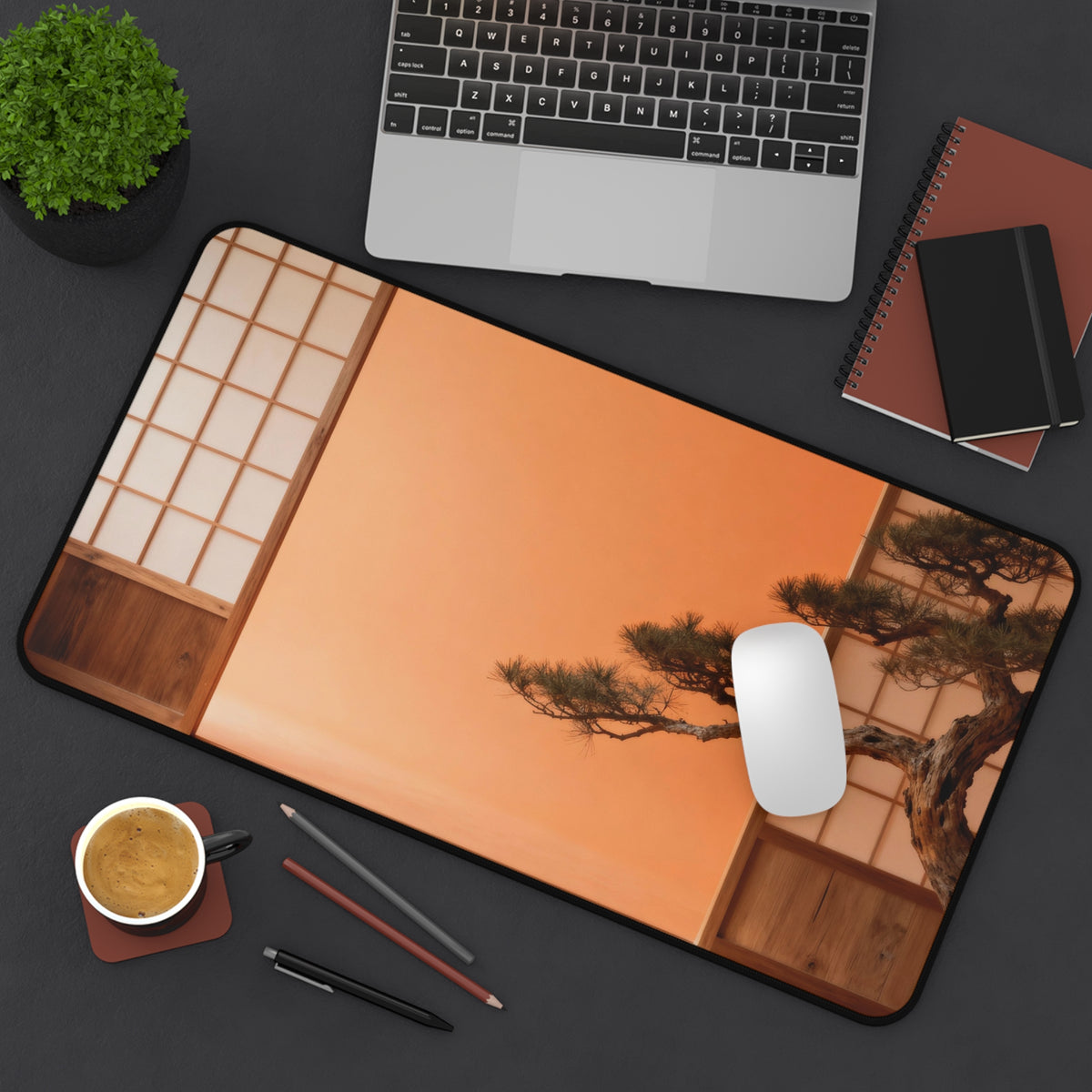 Desk setup with a mouse pad featuring a Japanese bonsai tree design, laptop, notebook, and coffee cup.