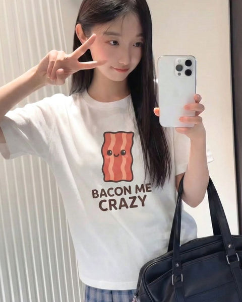 Young woman wearing a white t-shirt with a bacon graphic and text, holding a phone.