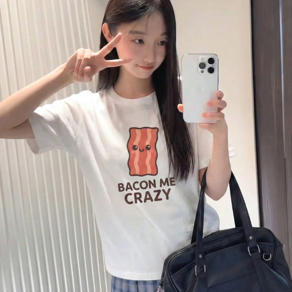 Young woman wearing a white t-shirt with a bacon graphic and text, holding a phone.