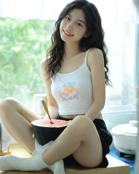 Woman wearing a bee t-shirt and sitting on a table with a bowl of watermelon in a bright room.