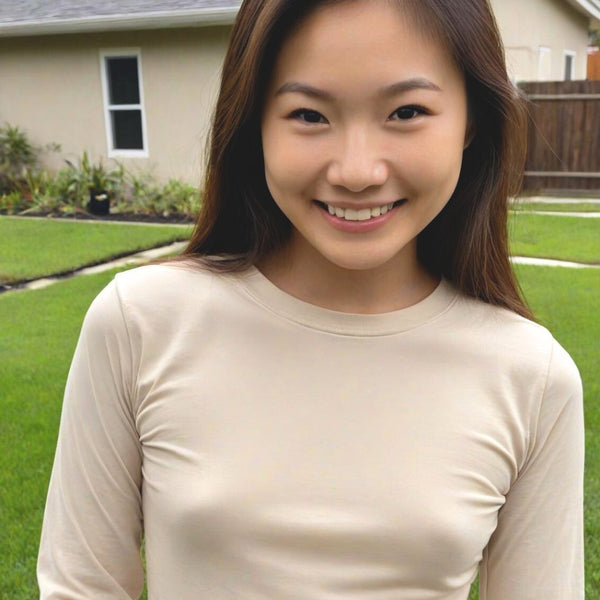 Woman wearing a beige long-sleeve shirt outdoors with a house and garden in the background