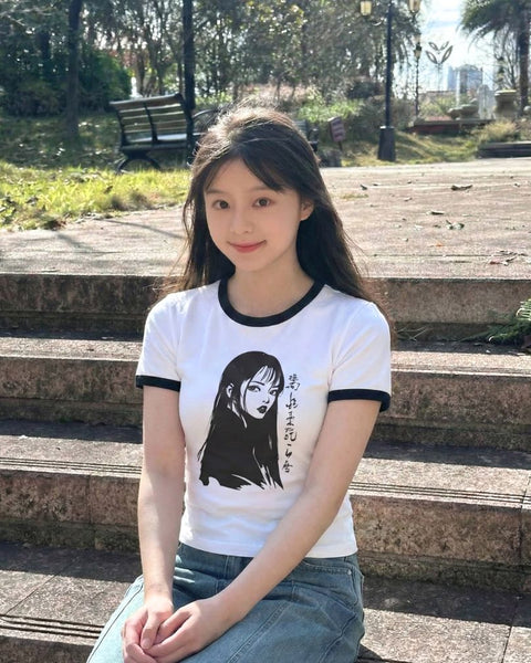 Woman wearing a white t-shirt with a manga design, sitting on steps outdoors.
