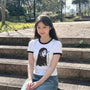 Woman wearing a white t-shirt with a manga design, sitting on steps outdoors.