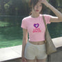 Person wearing a pink t-shirt with 'LOVE SPACES' text and a heart graphic, standing outdoors by a body of water.