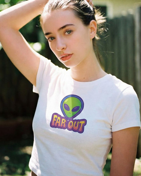 Woman wearing a white t-shirt with an alien graphic and 'FAR OUT' text outdoors.