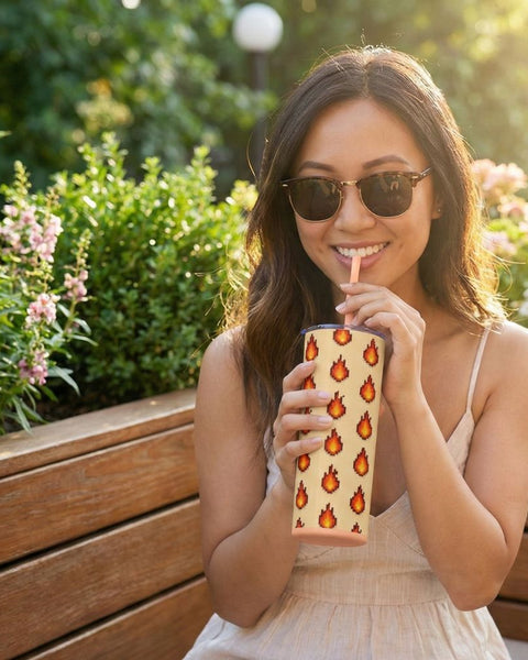 Woman drinking from a tumbler with a pixel art fire pattern outdoors