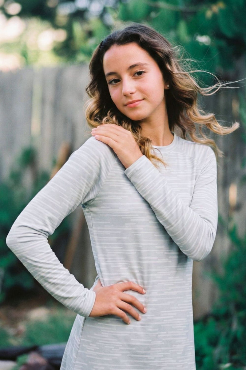 Woman wearing a light gray long-sleeve dress outdoors with greenery in the background