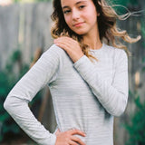 Woman wearing a light gray long-sleeve dress outdoors with greenery in the background