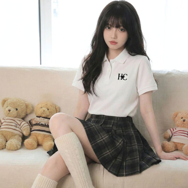 Woman in a white polo shirt with a Heart Circle logo and plaid skirt sitting on a couch with teddy bears.