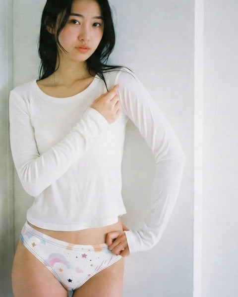 Woman wearing a white long-sleeve shirt and colorful underwear against a plain background