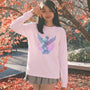 Woman wearing a pink sweatshirt with a  vaporwave graphic design outdoors among autumn leaves.