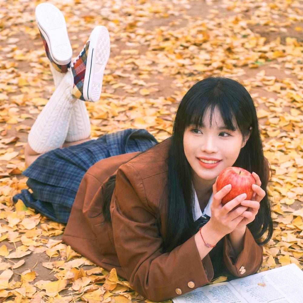 girl wearing plaid sneakers and school uniform laying on autumn leaves
