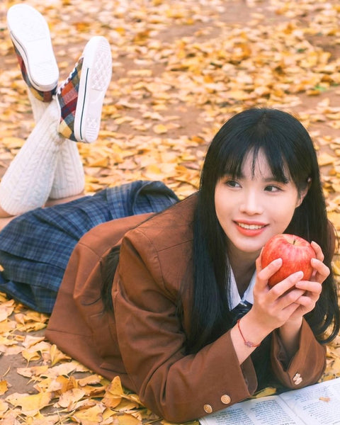 girl wearing plaid sneakers and school uniform laying on autumn leaves