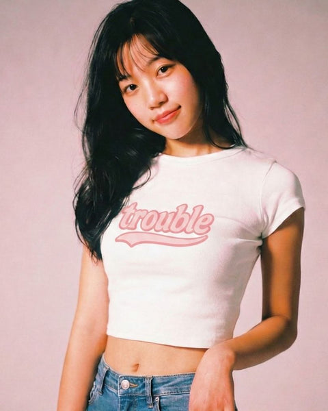 Woman wearing a white t-shirt with 'trouble' printed in pink on a plain background