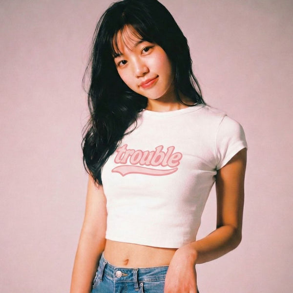 Woman wearing a white t-shirt with 'trouble' printed in pink on a plain background