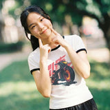 Woman wearing a white vintage anime t-shirt with a motorcycle graphic, posing outdoors.