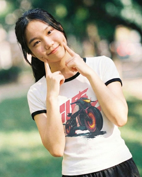 Woman wearing a white vintage anime t-shirt with a motorcycle graphic, posing outdoors.