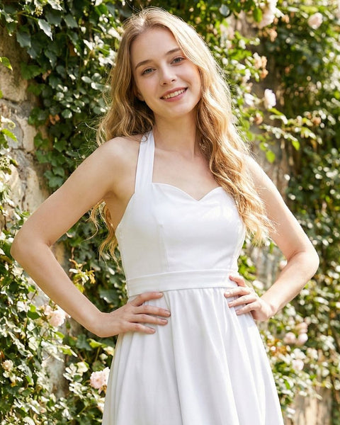 Woman in a white halter top dress standing against a green ivy-covered wall.