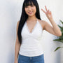 Cute asian woman wearing a white tie back top with lace and blue jeans, making a peace sign against a light background